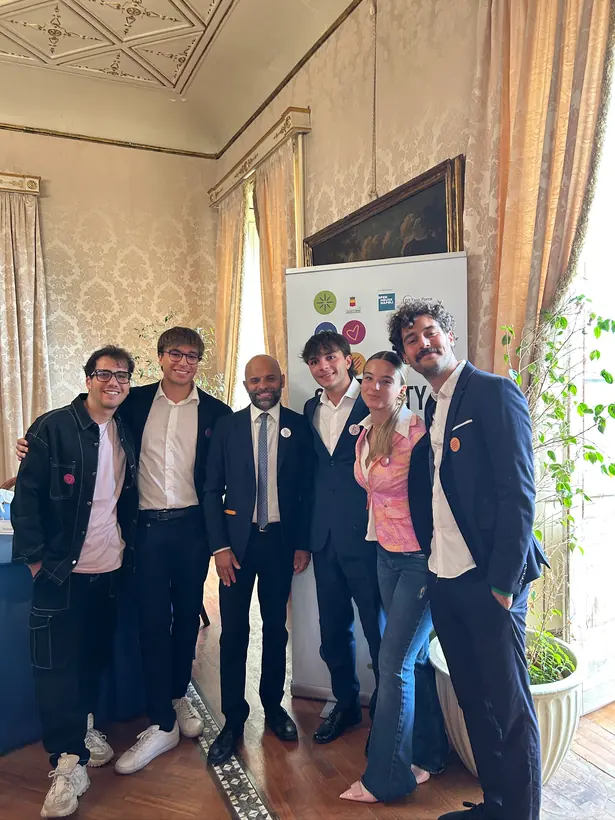 Il team in abito elegante a un evento a Napoli, davanti a un roll-up con i loghi dei partner.