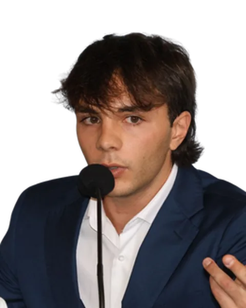 Giuseppe parla al microfono durante un evento, in giacca.